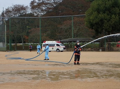 消防防災ヘリ着陸に備えてグラウンドへ散水する隊員