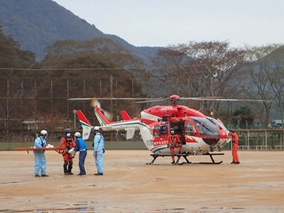 消防防災ヘリが着陸し航空隊員から救急隊員へ傷病者が引き継がれる